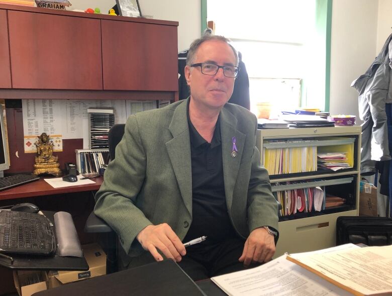 A man in a blazer sits at a desk