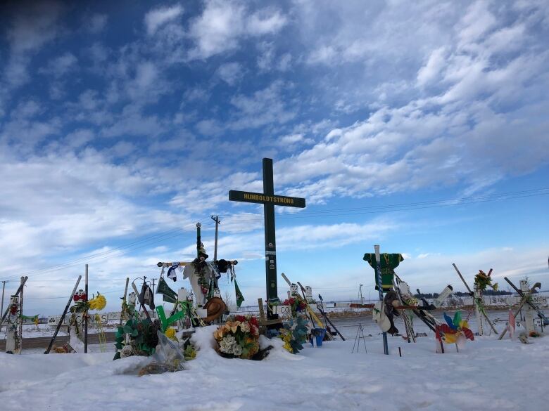 A memorial area is seen on a winterd ay. Crosses, jerseys, flowers and other mementos are seen on the ground.