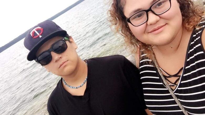 A teenage boy and girl are pictured posing for a selfie in front of a lake.