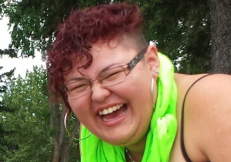 A young woman is pictured laughing while kneeling down with green fabric wrapped loosely around her neck.