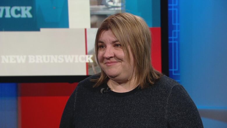 A woman with short, straight brown hair and wearing a black long-sleeved shirt sits in CBC New Brunswick's studio, looking off to the left of the photo.