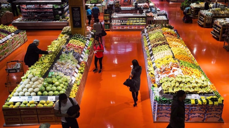 People walk around a produce section in a grocery store.