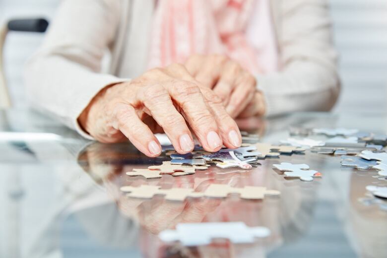 Close up on hands of older woman working on a jigsaw puzzle.