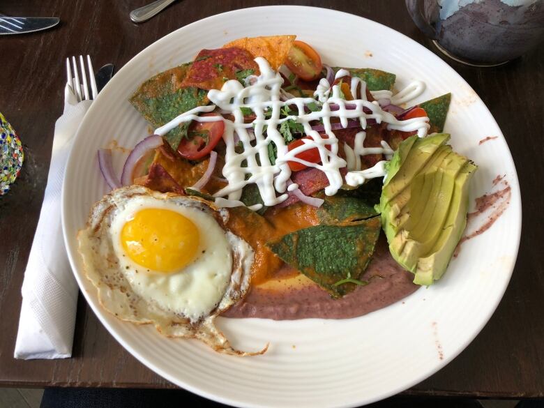 A plate covered in tortilla chips, a fried egg, sliced avocado and an orangey-red sauce.