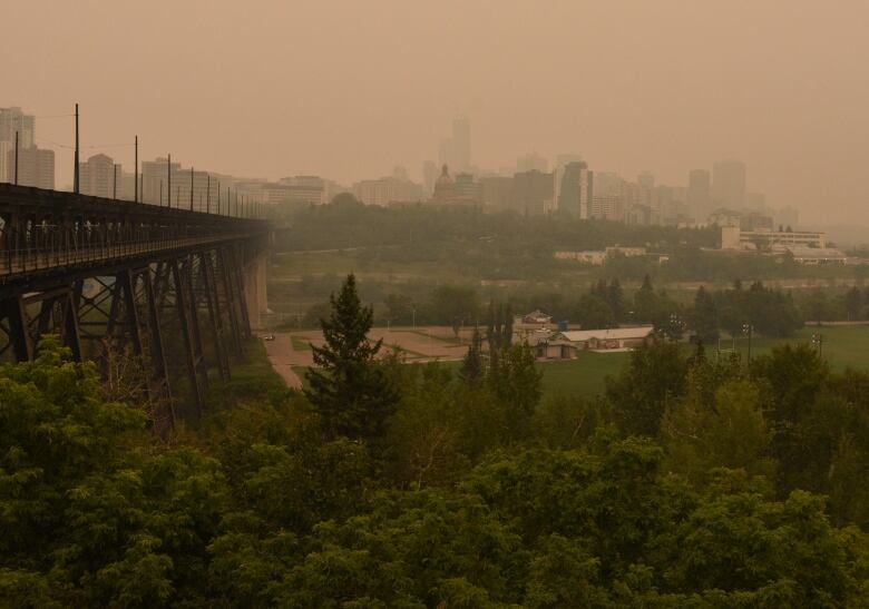 An old black bridge and green river valley below a hazy yellow sky.