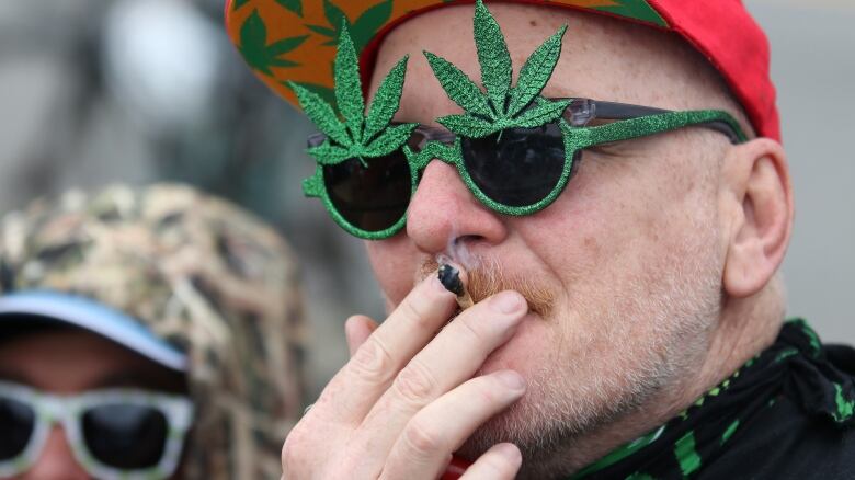 A man wearing novelty cannabis sunglasses smokes a joint at Vancouver's 4/20 event in 2018.