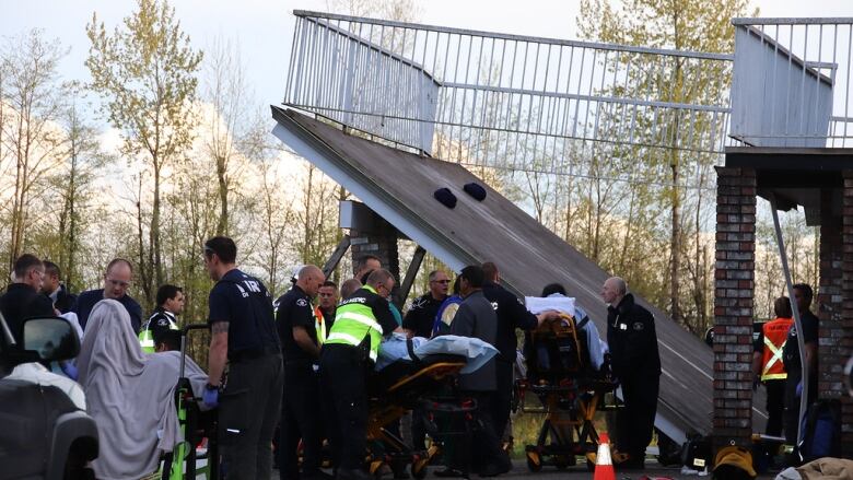 A crowd of paramedics tend to patients on stretchers next to a collapsed deck on a home.