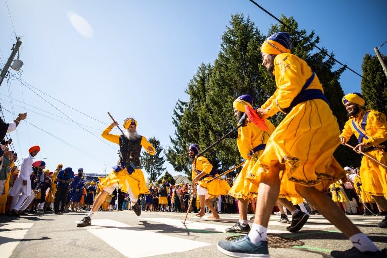 People in brightly-coloured attire sing and dance on city streets.