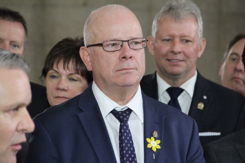 A man with glasses wearing a suit stands in a crowd of people.