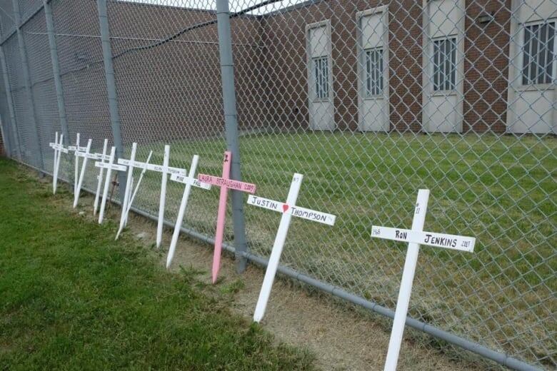 Crosses with the names of inmates who died rest against a fence at London's Elgin-Middlesex Detention Centre.