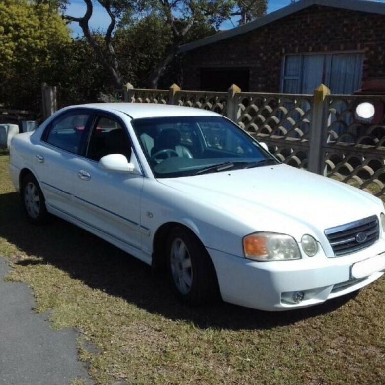 A white sedan is parked in a driveway in front of a small house. 