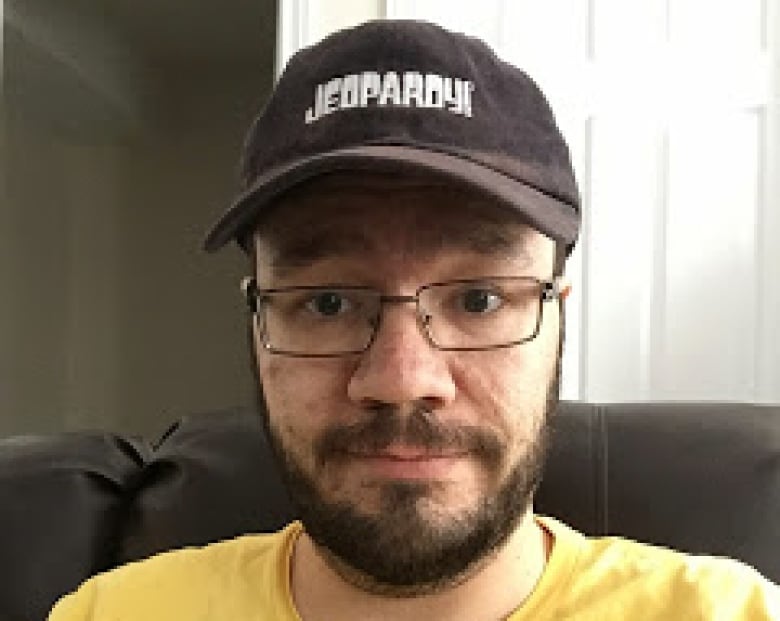 A man in a Jeopardy hat poses for a photo.