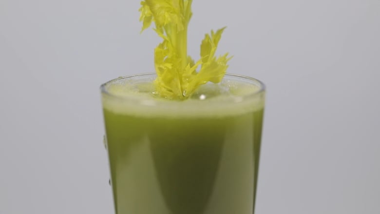 Celery leaves stick out from the top of a glass filled with green juice.