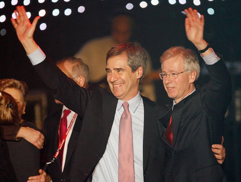 Two men stand and wave at a crowd.