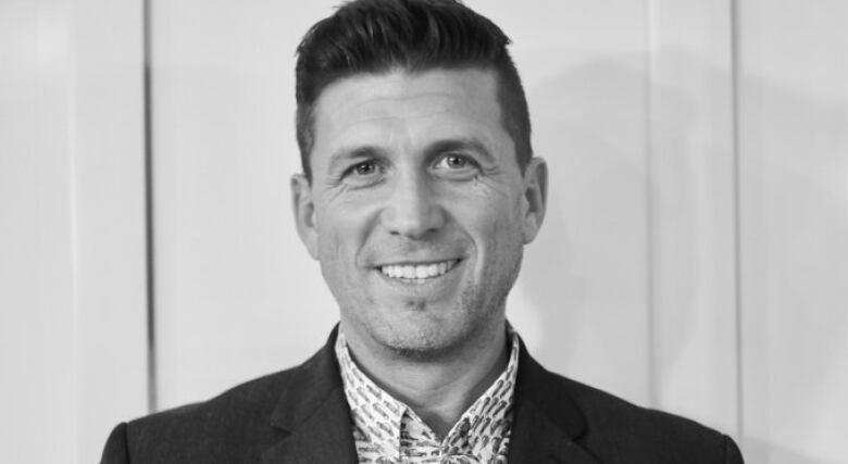 A black and white photo of a young man with short hair smiling at the camera,