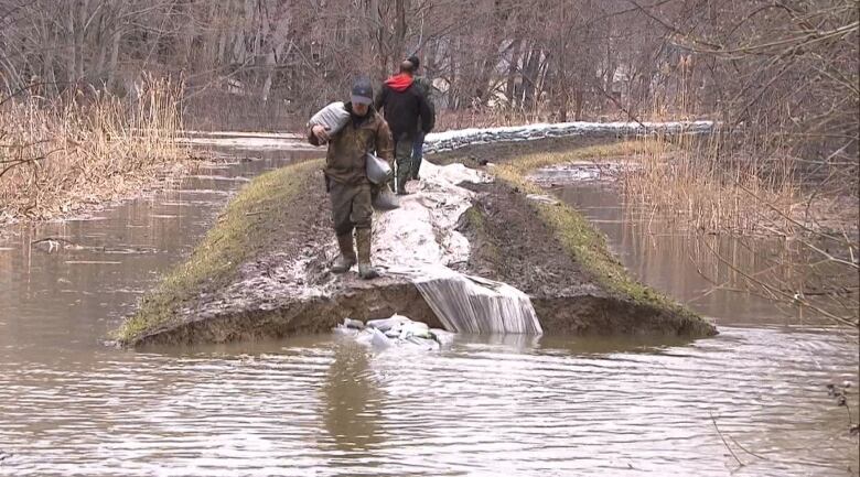 People standing around high levels of water dropping sandbags and dirt into it. 