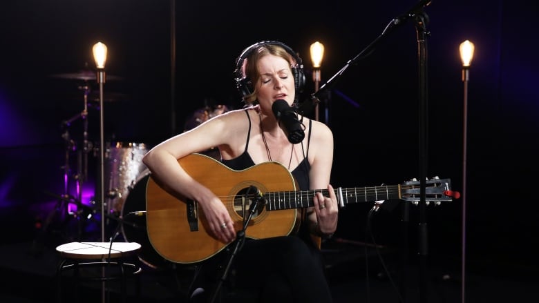 A singer with red hair and black clothing performs on an acoustic guitar.