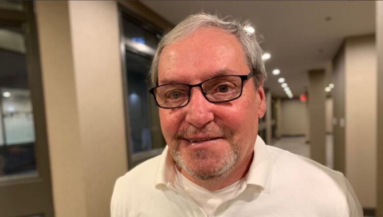 A grey haired man with glasses looks into the camera