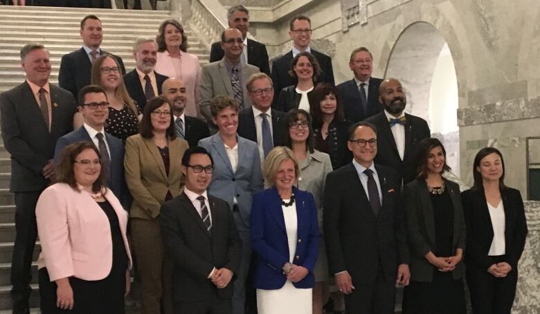 A group of politicians stand on the steps inside Alberta's legislature.