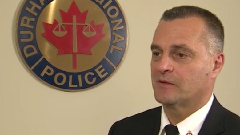 Man in suit beside Durham Regional Police Service Logo