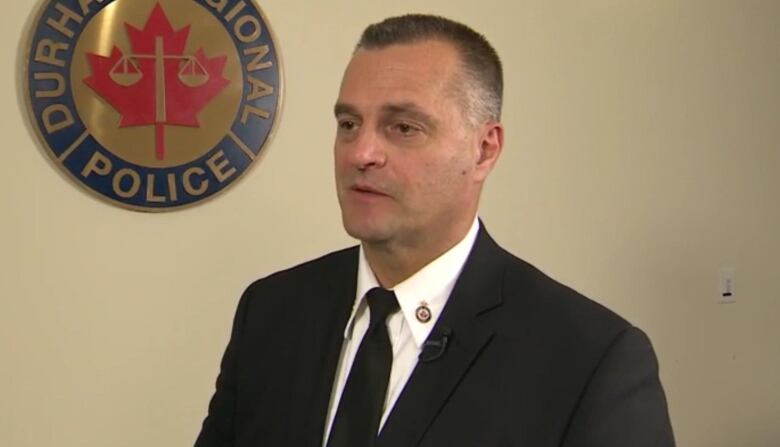 Man in suit beside Durham Regional Police Service Logo