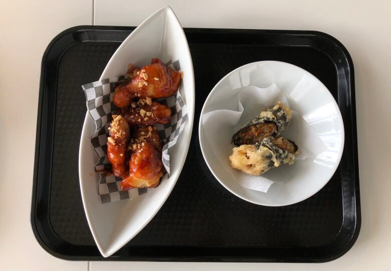 A bowl of chicken wings covered in a bright red sauce, and a bowl with a cut fried roll.