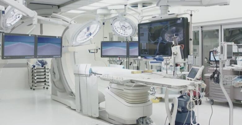 An operating table surrounded by large lights, monitors and other pieces of equipment in a spacious room.