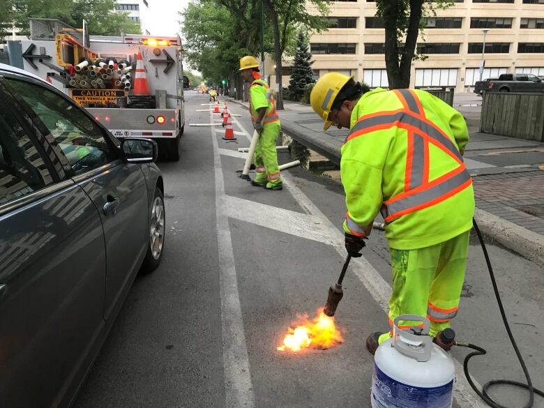 City worker has blow torch and is torching the road