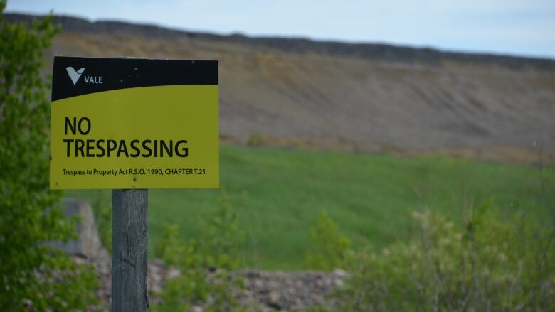 A no trespassing sign in front of a green hill.