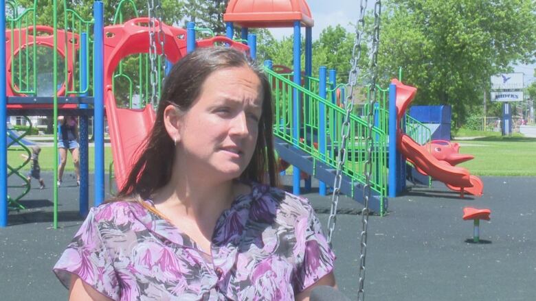 A woman in a pink and purple patterned shirt pictured in front of a brightly-coloured playground. 