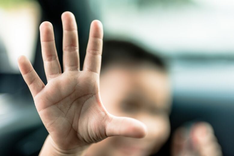 A child's hand is shown in closeup, in front of their obscured face.