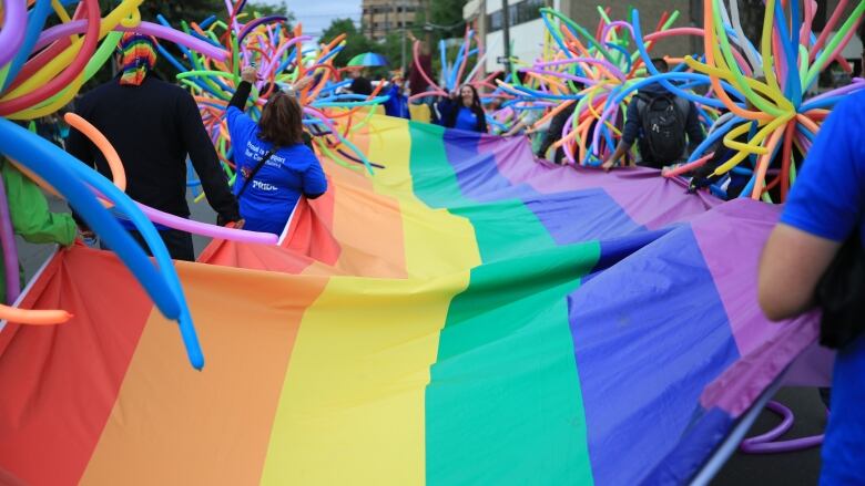 A long rainbow flag is held by people marching in a Pride parade.