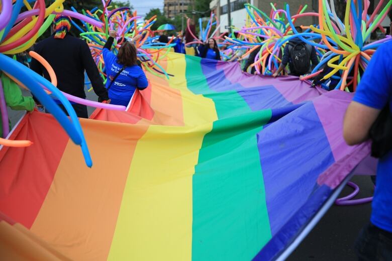 A long rainbow flag is held by people marching in a Pride parade.