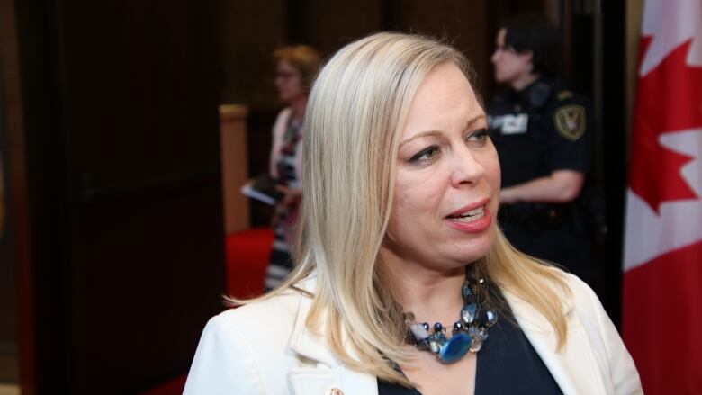 A woman speaks with a Canadian flag in the background.