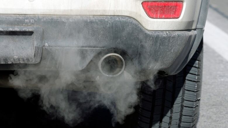 Close-up shot of a silver car tailpipe with exhaust.