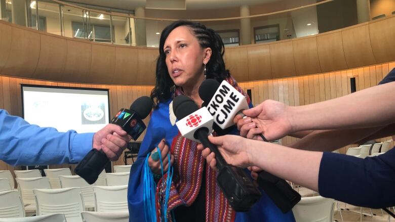 A woman in a Metis sash is interviewed by several media outlets.