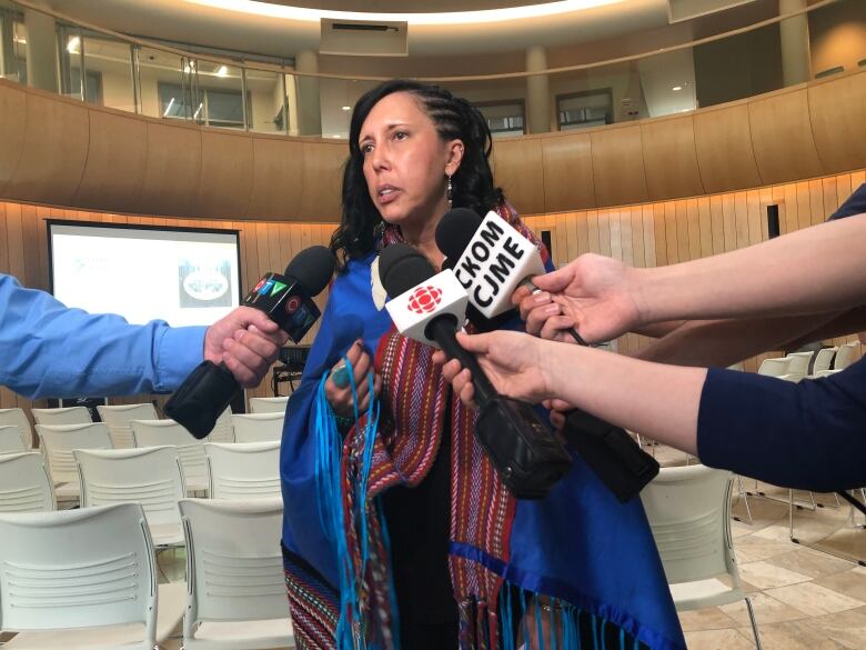 A woman in a Metis sash is interviewed by several media outlets.