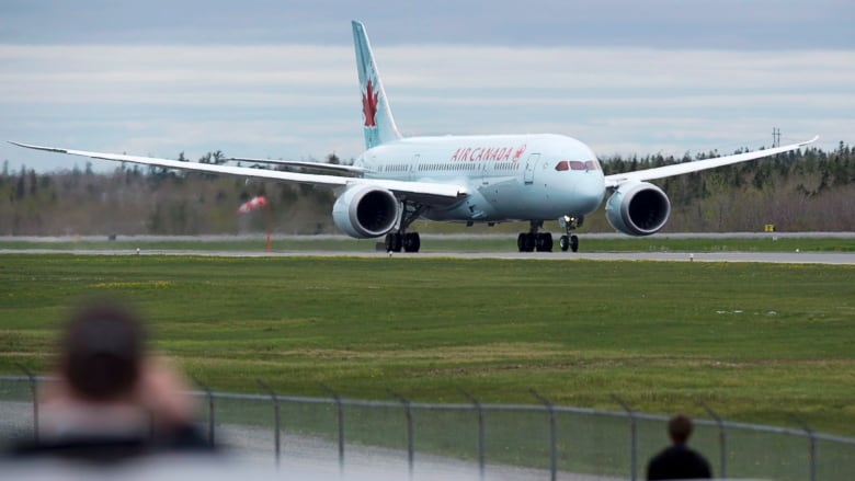 A large white plain with the words Air Canada in red lettering lands on a paved runway, with grass in the foreground