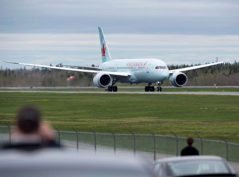 A large white plain with the words Air Canada in red lettering lands on a paved runway, with grass in the foreground