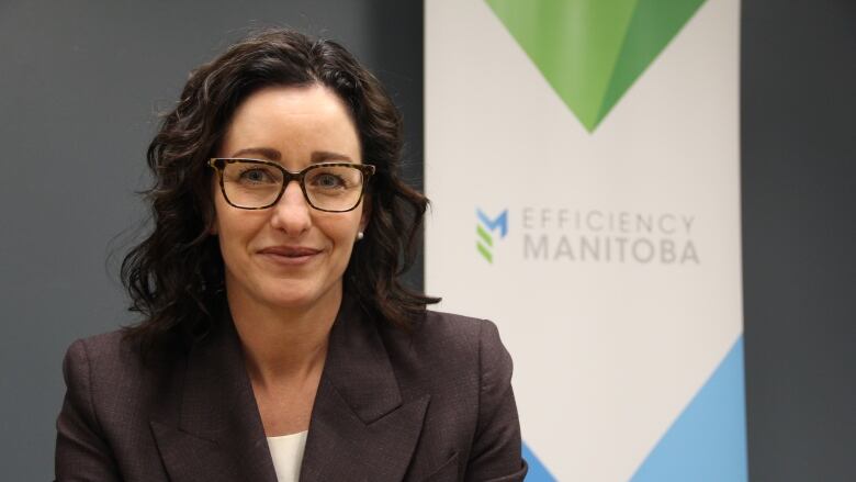 A woman in a blazer is seated behind a banner with the 'Efficiency Manitoba' logo on it.