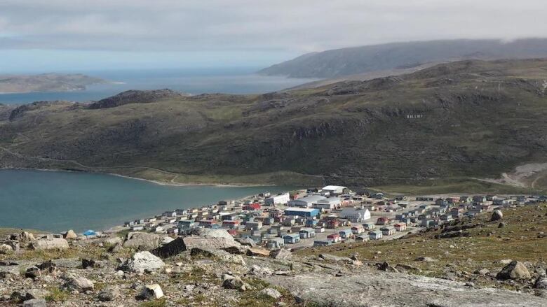 An aerial view of a small community by water, surrounded by rolling tundra.