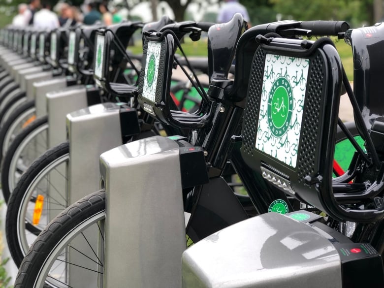 A closeup of a bike share rack in day time. about a dozen bikes are pictured docked.