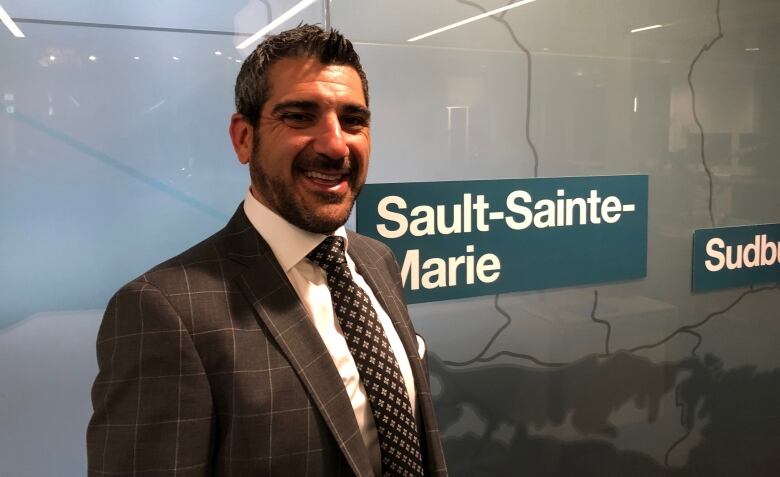 Bearded, smiling man stands in front of map identifying Sault Ste Marie