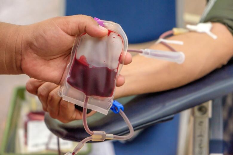 A health care worker holds up a bag of blood from a donor. 