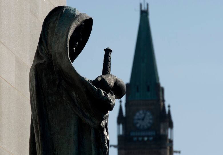 A statue holding a sword stands in front of a clocktower in Ottawa.