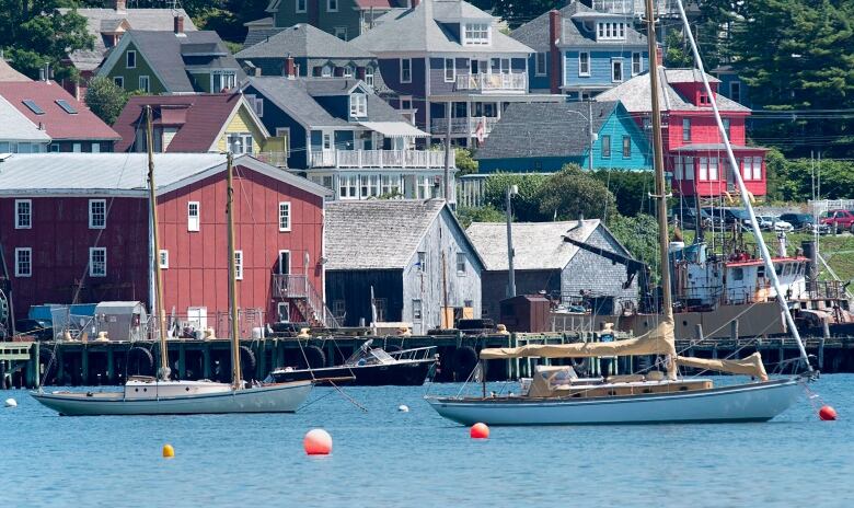 The Lunenburg waterfront is seen with sailboats moored in blue water and wooden buildings on the wharf.