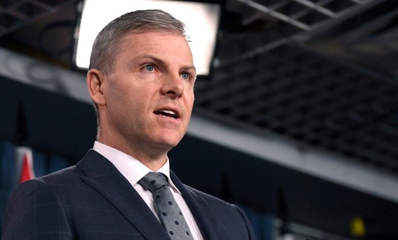 A man in a suit gestures with his hands as he speaks.