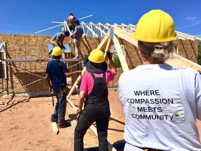 People in hard hats carry lumber towards a partially built house