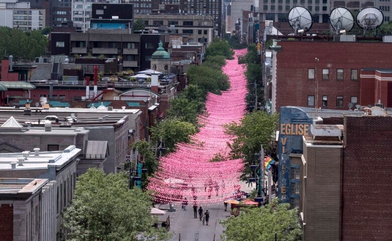 Pink strings of light cover Ste-Catherine Street in Montreal, bordered by trees on each side.