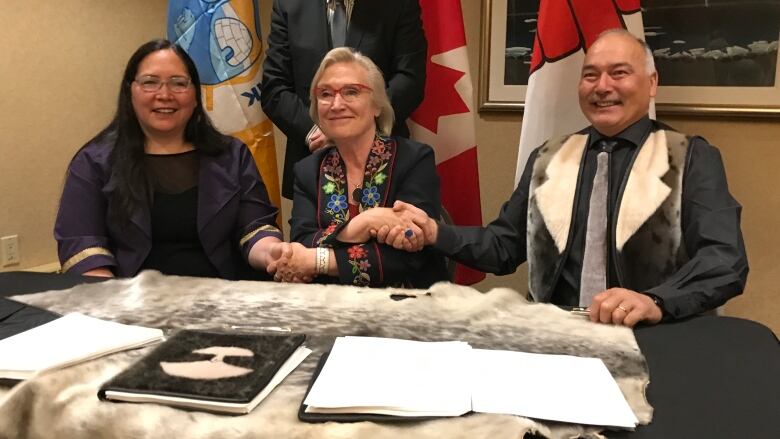 Three people shake hands, with two women on the left and one man on the right. 